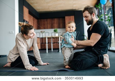 Young Parents Sitting On A Yoga Mat, Spending Time With Their Infant Baby
