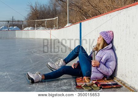 Lovely Young Woman Relaxing After Riding Ice Skates And Drinking Hot Drink From Termo Pot On The Ice