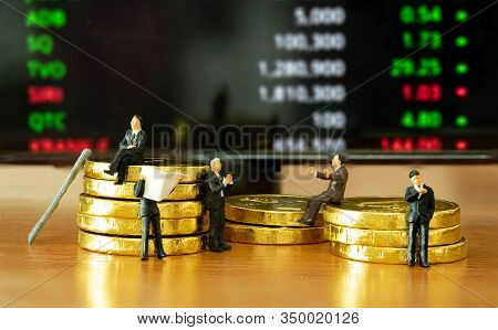 The Miniature Figure A Group Of Business Men Sitting On Top Of Pile Stack Of Golden Coins And Some S