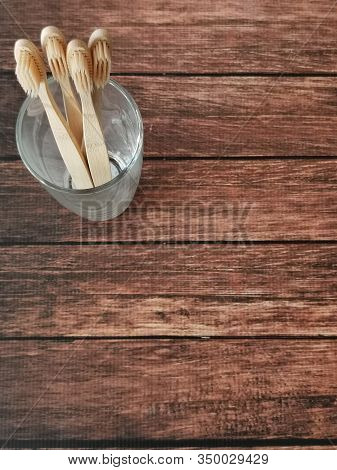 A Family Set Of Four Wooden Toothbrushes In A Glass On Wooden Background With Copy Space