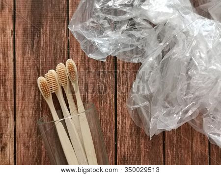 A Family Set Of Four Wooden Toothbrushes In A Glass On Wooden Background With Polyethylene