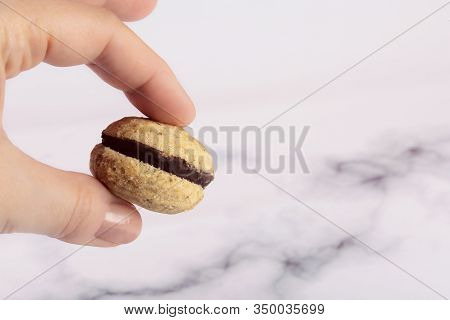 Female Hand Holds A Cookie Called Bacio Di Dama On A Marble Background