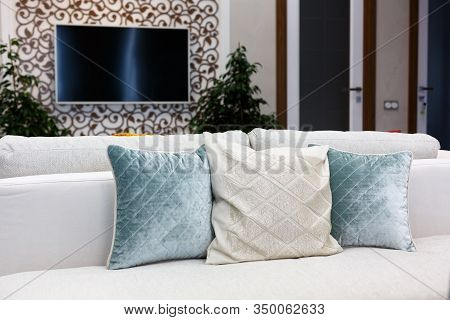 Red, blue and brown pillows on a white sofa, living room interior. A white TV is hanging on the wall.