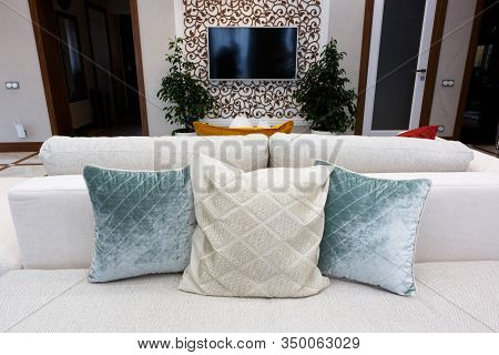 Blue and white pillows on a white sofa, living room interior. A white TV is hanging on the wall.