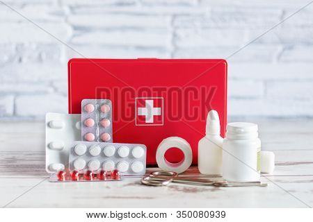 First Aid Kit Red Box With Medical Equipment And Medications For Emergency On White Wooden Backgroun