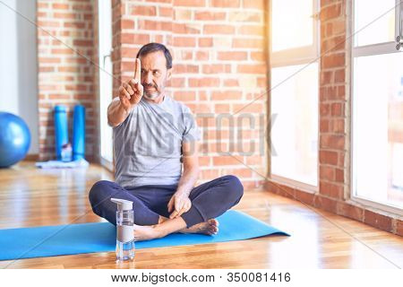 Middle age handsome sportman sitting on mat doing stretching yoga exercise at gym Pointing with finger up and angry expression, showing no gesture