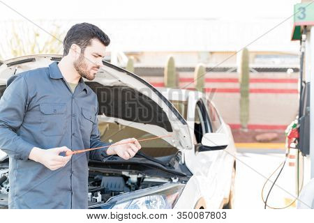 Confident Male Worker Checking Engine Oil With Dipstick At Gas Station