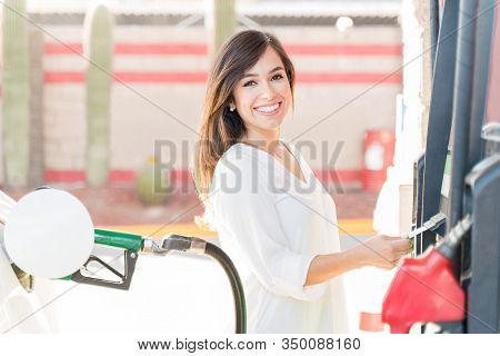 Portrait Of Happy Woman Operating Fuel Pump Machine At Gas Station