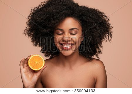 Attractive Black Female With Clean Skin Laughing With Closed Eyes And Showing Half Of Fresh Orange W