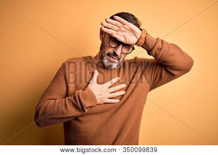 Middle age hoary man wearing brown sweater and glasses over isolated yellow background Touching forehead for illness and fever, flu and cold, virus sick