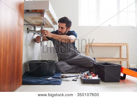 Male Plumber Working To Fix Leaking Sink In Home Bathroom