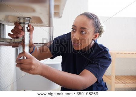 Female Plumber Working To Fix Leaking Sink In Home Bathroom