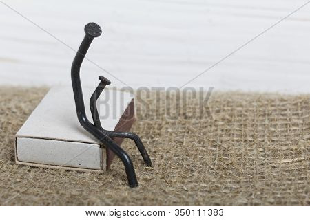 Figurines Of Man Made Of Carpentry Nails. Sit On A Box Of Matches, Next To Each Other.