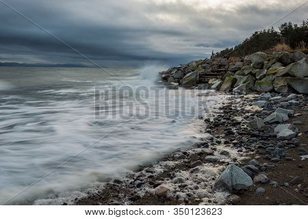 Stormy Morning Along A Rocky Beach With Dramatic Waves Hitting Rocks.