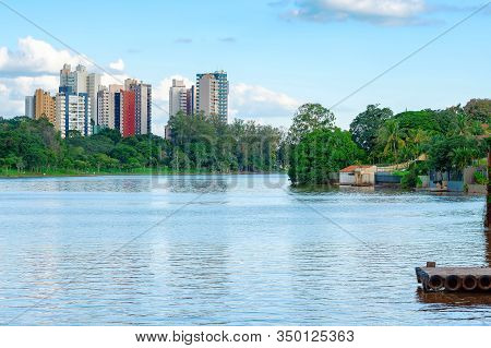 View Of A Lake With Trees On The Lake Shore And Few Buildings Of The City On The Background. City Wi