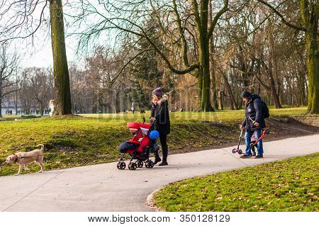 Poznan, Poland - February 9, 2020: Woman And Father Walking With Kid And Dog On A Footpath Along Gre