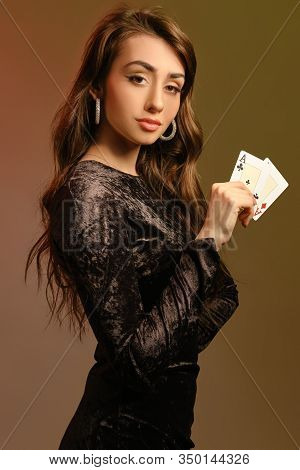 Brunette Lady In Black Velvet Dress And Jewelry Showing Two Aces, Posing Sideways On Colorful Studio