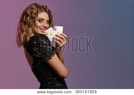Brown-haired Maiden In Black Dress Is Smiling, Showing Two Aces, Posing Sideways On Colorful Backgro