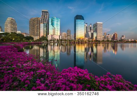 Lake With Purple Flowers In City Park Under Skyscrapers At Twilight. Benjakiti Park In Bangkok, Thai