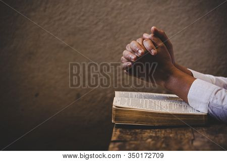 Hands Folded In Prayer On A Holy Bible In Church Concept For Faith