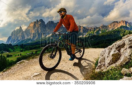 Tourist cycling in Cortina d'Ampezzo, stunning rocky mountains on the background. Man riding MTB enduro flow trail. South Tyrol province of Italy, Dolomites.