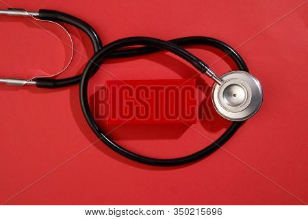 black stethoscope on a red background top view with copy space.