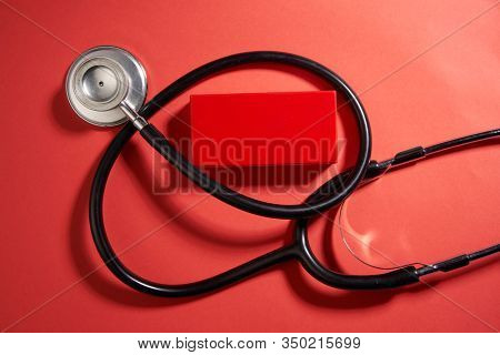 black stethoscope on a red background top view with copy space.