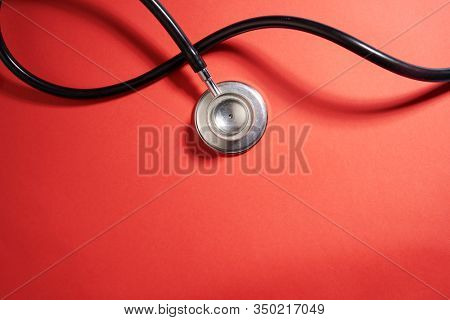 black stethoscope on a red background top view with copy space.