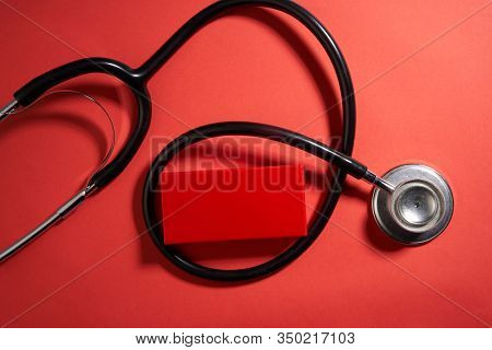 black stethoscope on a red background top view with copy space.