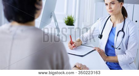 Doctor and patient discussing medical problems in a hospital consulting room. Doc filling in a patient's form
