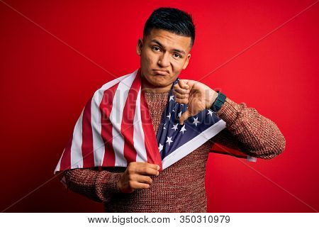Young handsome latin patriotic man wearing united states of america falg with angry face, negative sign showing dislike with thumbs down, rejection concept