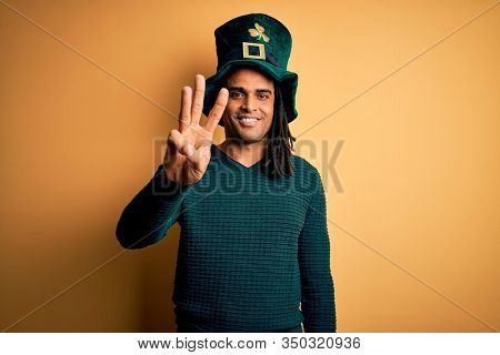 Young african american man wearing green hat with clover celebrating saint patricks day showing and pointing up with fingers number three while smiling confident and happy.