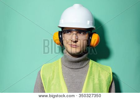Studio Portrait Of Young Confident Engineer Wearing Safety Equipment On Background Of Aqua Menthe Co