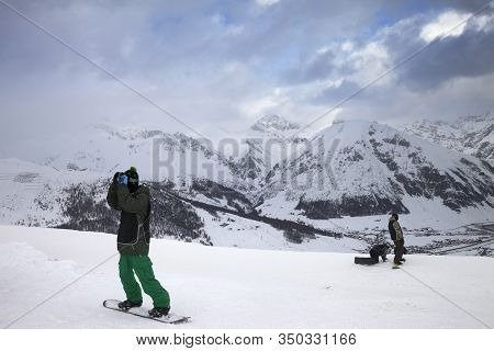 Group Of Snowboarders Starts On Off-piste Descent. High Snowy Mountains And Cloudy Storm Sky At Wint