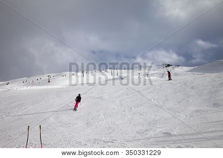 Snowy Ski Slope With Skiers In High Mountains And Cloudy Sunlit Sky At Winter Day. Ski Area Mottolin