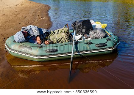 Tuzha, Russia - June 13, 2019: Fisherman Sleeps In A Boat On A River Near The Shore. Pizhma River