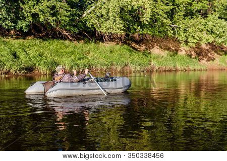 Tuzha, Russia - June 14, 2019: A Man Catches Fish On The River, A Fisherman On A Rubber Boat Floats 