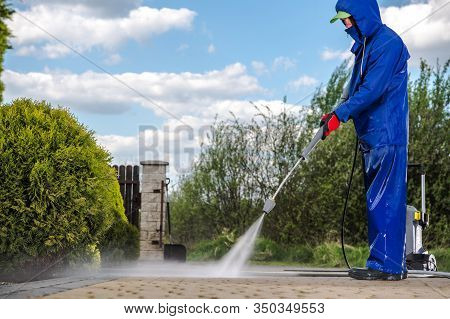 Men In Blue Rain Coat Cleaning His Driveway Using Pressure Washer.