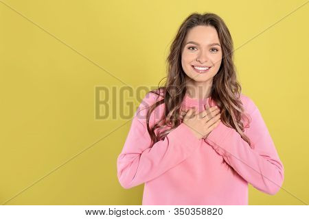 Beautiful Grateful Woman With Hands On Chest Against Yellow Background. Space For Text