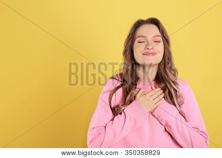 Beautiful Grateful Woman With Hands On Chest Against Yellow Background. Space For Text