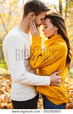 Image of attractive young caucasian couple in love hugging while walking at autumn park