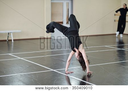 Young female dancer wearing black outfit doing difficult handspring element, horizontal shot