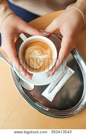 Woman Hands Holding Cup Of Cappuccino, Top View. Morning Mood With Coffee. Coffee Shop. Girl Enjoyin