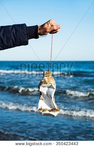 closeup of a man holding a fishing line with a used plastic bottle in the fish hook, freshly fished in the ocean, in front of the water