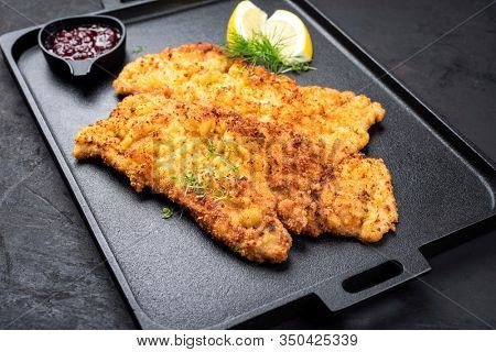 Traditional deep fried Wiener schnitzel from veal topside with cranberry jam and lemon slices offered as top view on a black modern design tray 