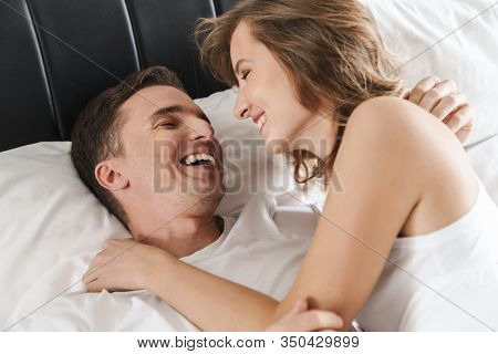 Attractive smiling young couple laying in bed in the bedroom at home, embracing