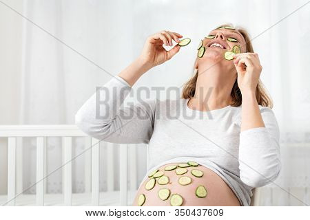 Caucasian Pregnant Woman Sitting On A Chair And Putting Cucumber Slices On Her Face And Belly, Spa D