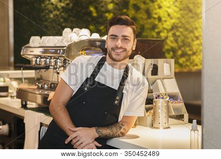 Barista Career. Cheerful Coffeemaker Guy In Uniform Posing Near Coffee-machine Standing In Cafe