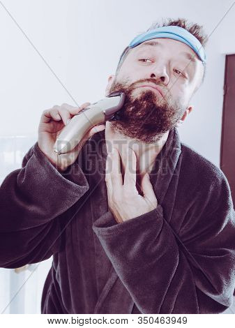 Bearded Man Looking At Himself In Mirror Trimmng, Shaving His Beard Using Electric Timmer Razor. Guy