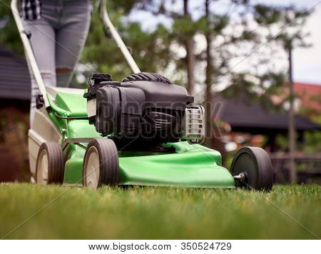 Close Up Of Female Legs In Jeans Of Woman Using Lawn Mower On Backyard. Selective Focus Of Incognito